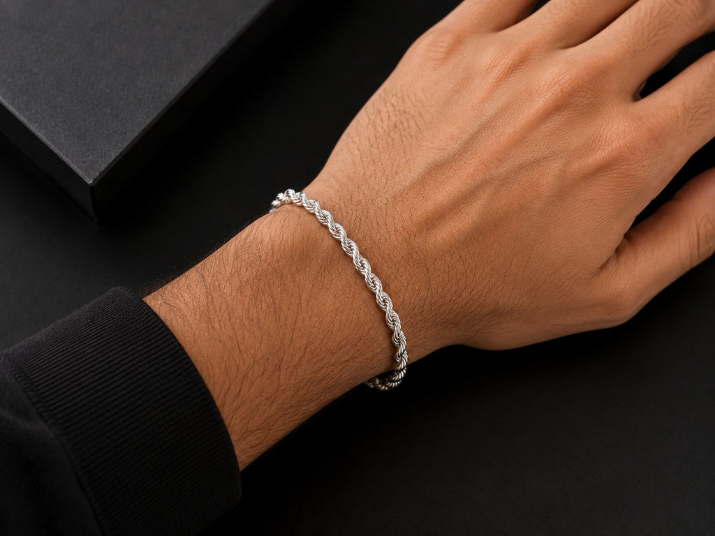 A silver braided chain bracelet worn on a person's wrist, shown against a dark background with a black box partially visible.