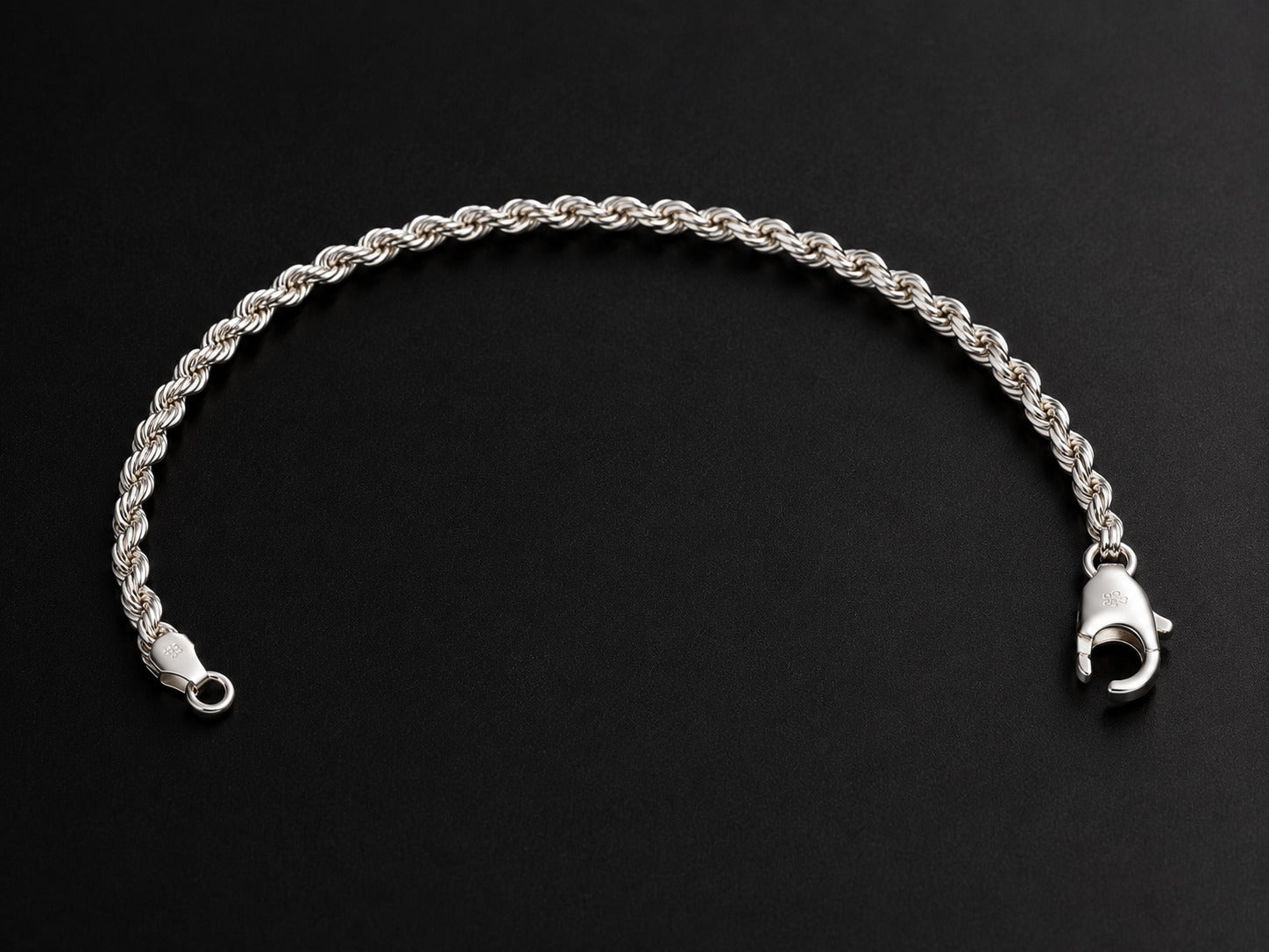 A silver rope chain bracelet with a lobster clasp, displayed on a dark black background.