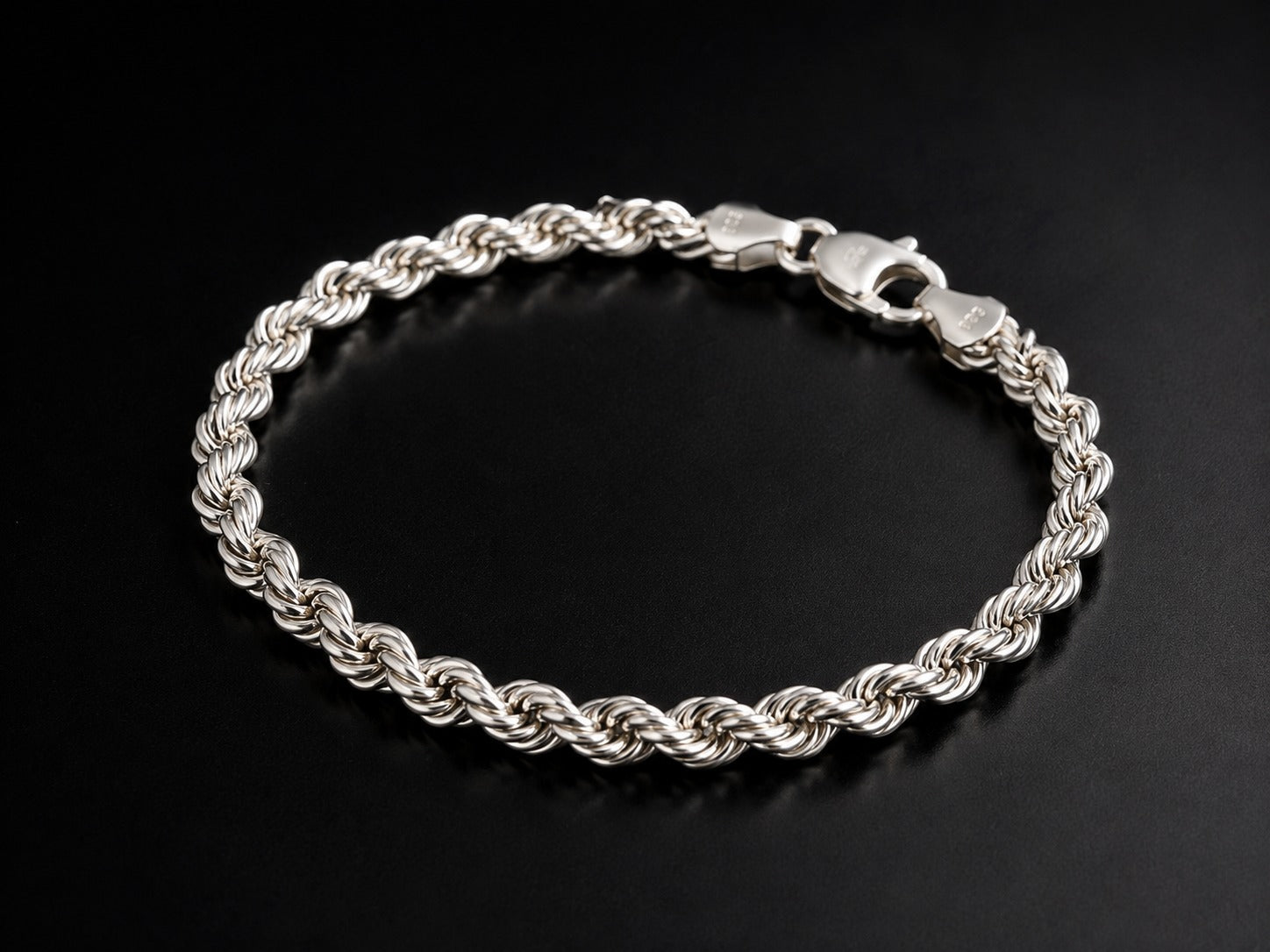 A silver twisted rope chain bracelet with a lobster clasp, displayed on a dark black background.