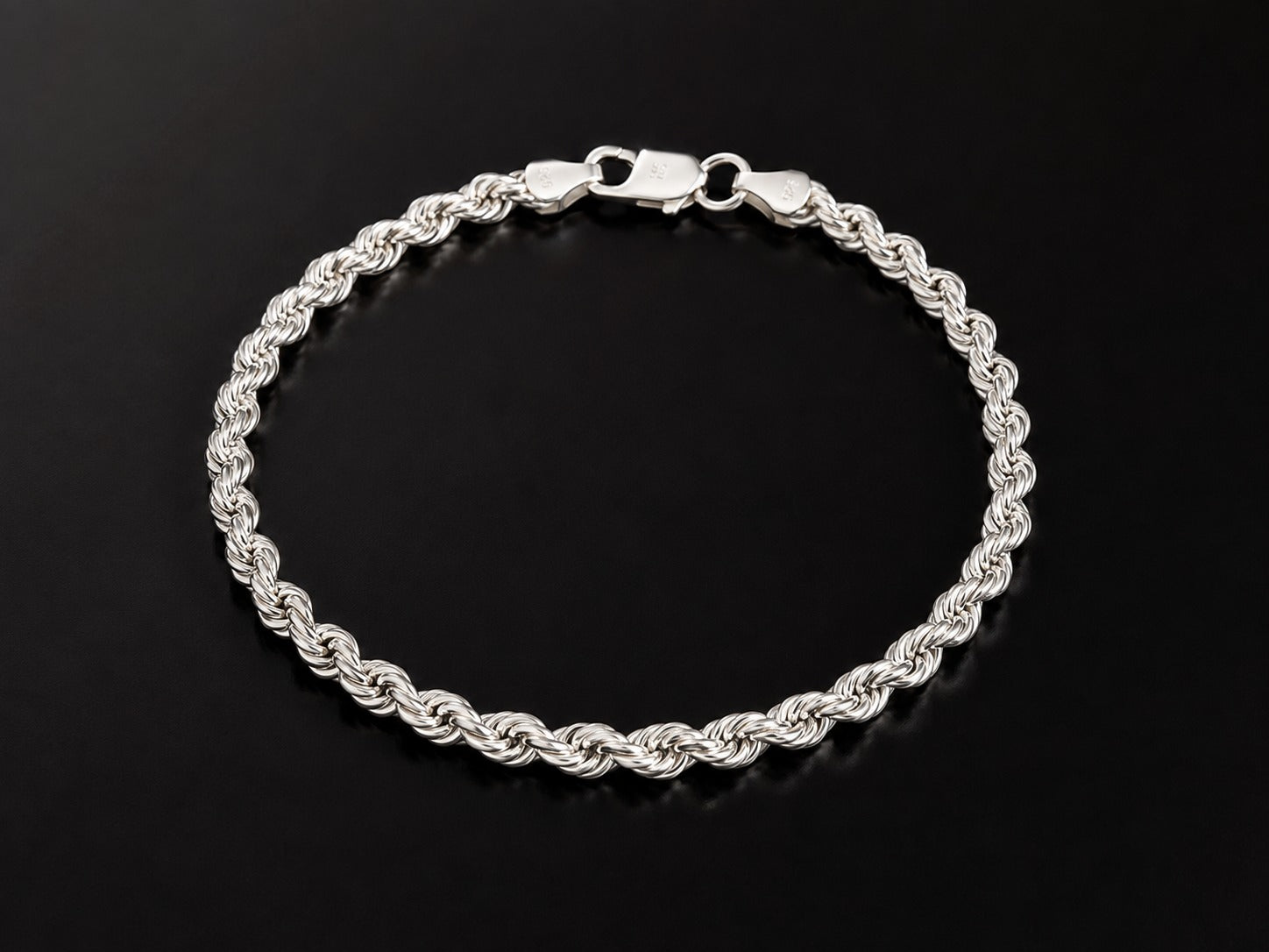 A silver-toned twisted rope chain bracelet with a lobster clasp, displayed on a reflective black surface.