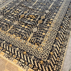 Close-up of a black and cream Afghan Khotan wool rug showing its woven pattern and product label.