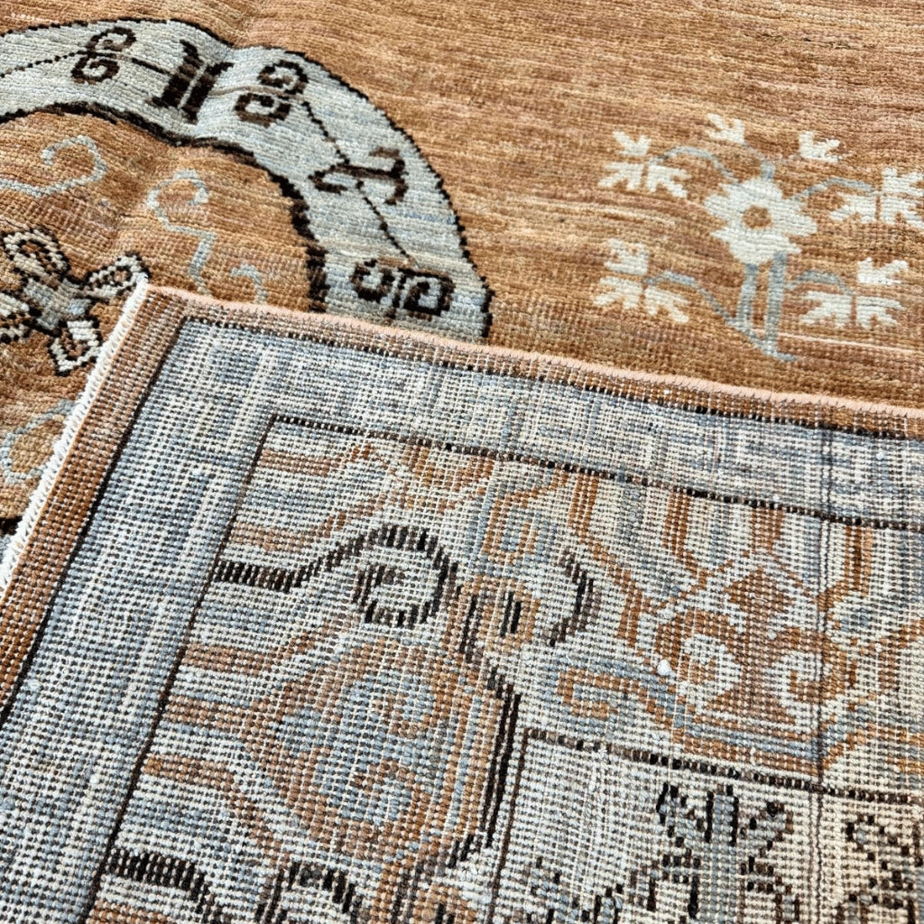 Close-up of a traditional circular medallion with dark geometric designs against the warm brown field of a Khotan-inspired rug.