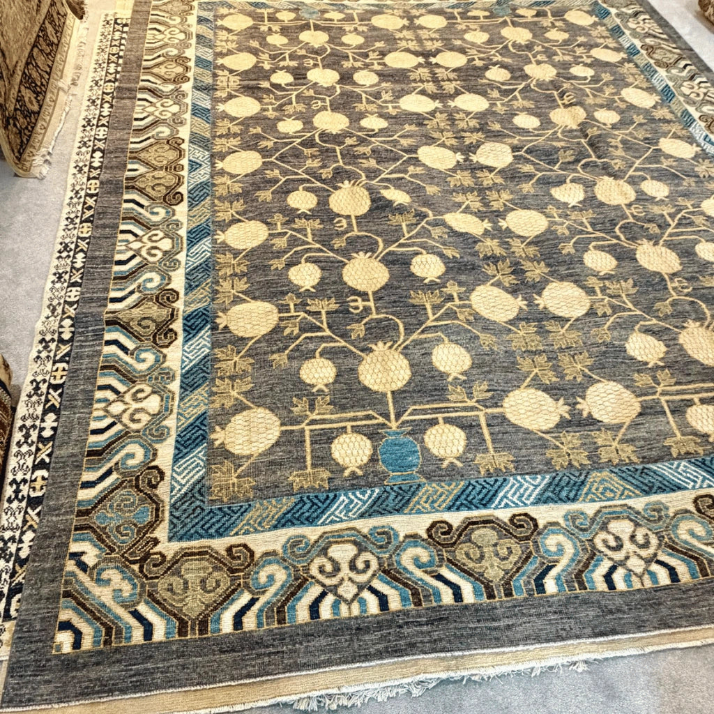 Traditional Afghan Khotan rug featuring repeating cream pomegranate tree motifs on a charcoal grey wool field.
