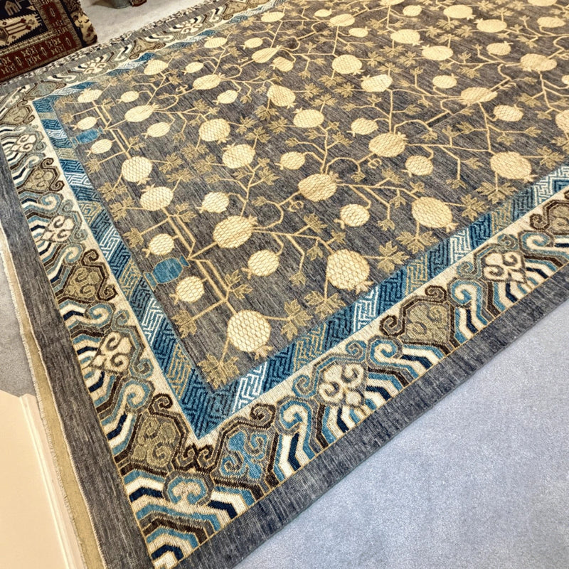 Traditional Khotan wool rug showing its charcoal grey background, cream botanical motifs, and multicolor decorative borders.