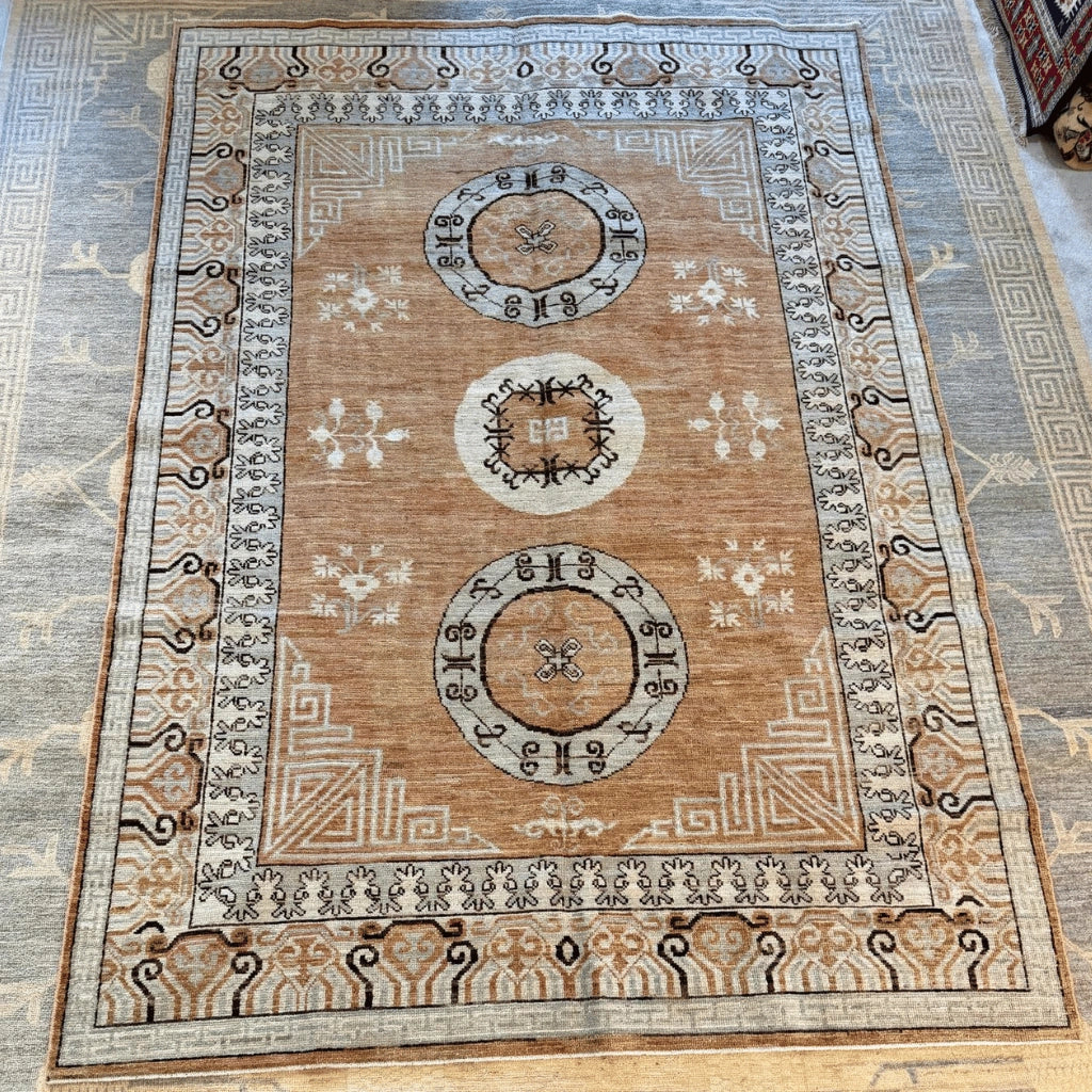 Afghan hand-knotted Khotan wool rug in tan, warm brown, and cream with three traditional medallions and intricate geometric borders.