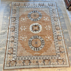 Afghan hand-knotted Khotan wool rug in tan, warm brown, and cream with three traditional medallions and intricate geometric borders.