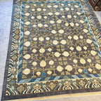Afghan hand-knotted Khotan wool rug with charcoal grey field, cream pomegranate tree motifs, and blue geometric borders.