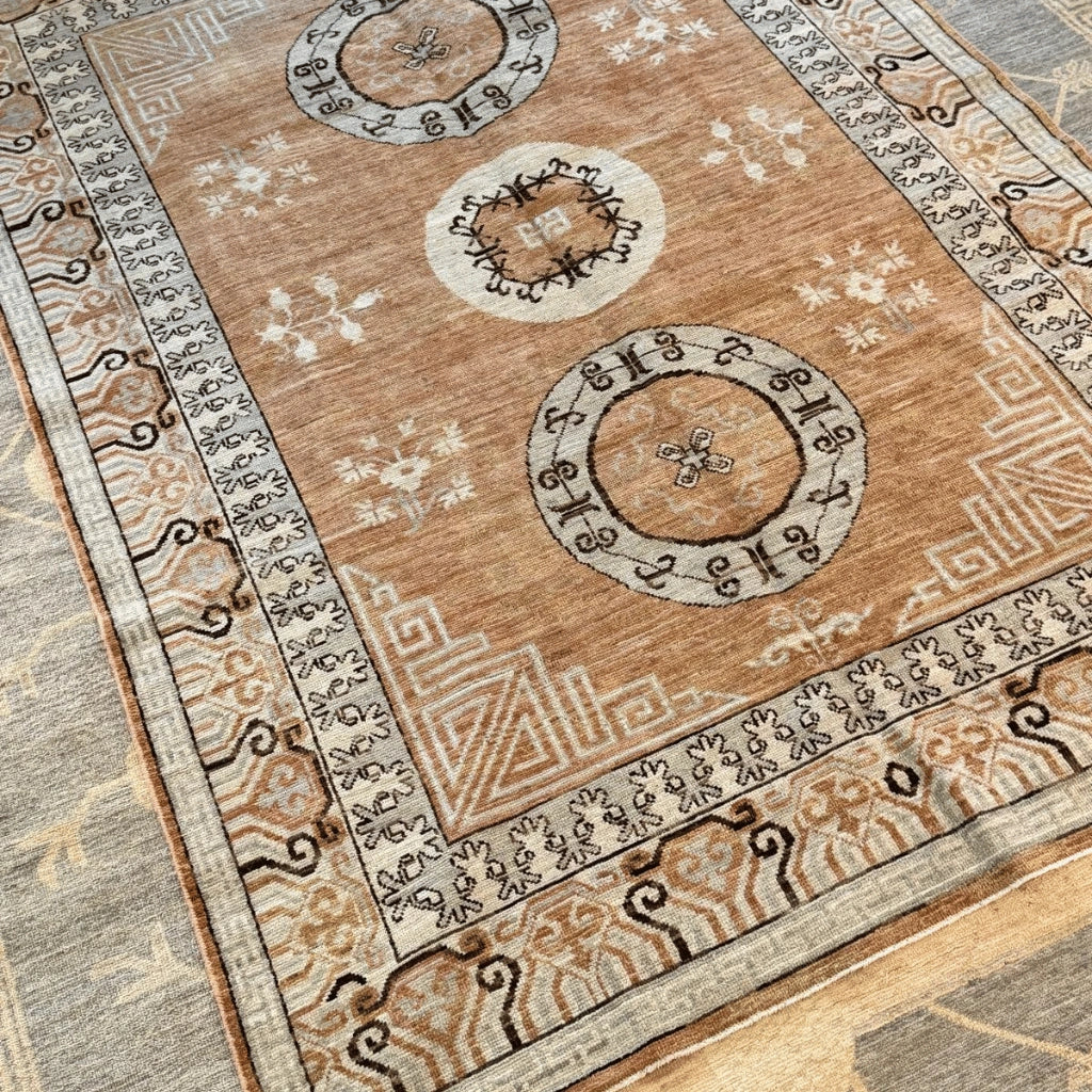 Intricate cream and beige rug border featuring dark geometric motifs on a traditional Afghan-inspired wool area rug.