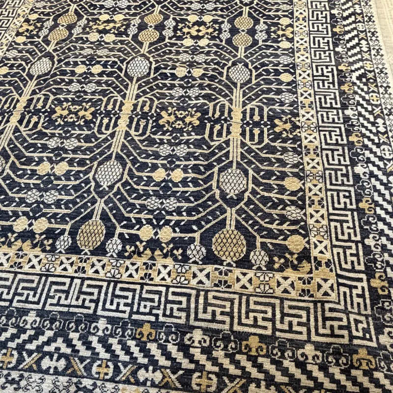 Angled view of a black and cream Afghan Khotan handmade wool rug with intricate traditional geometric patterns.