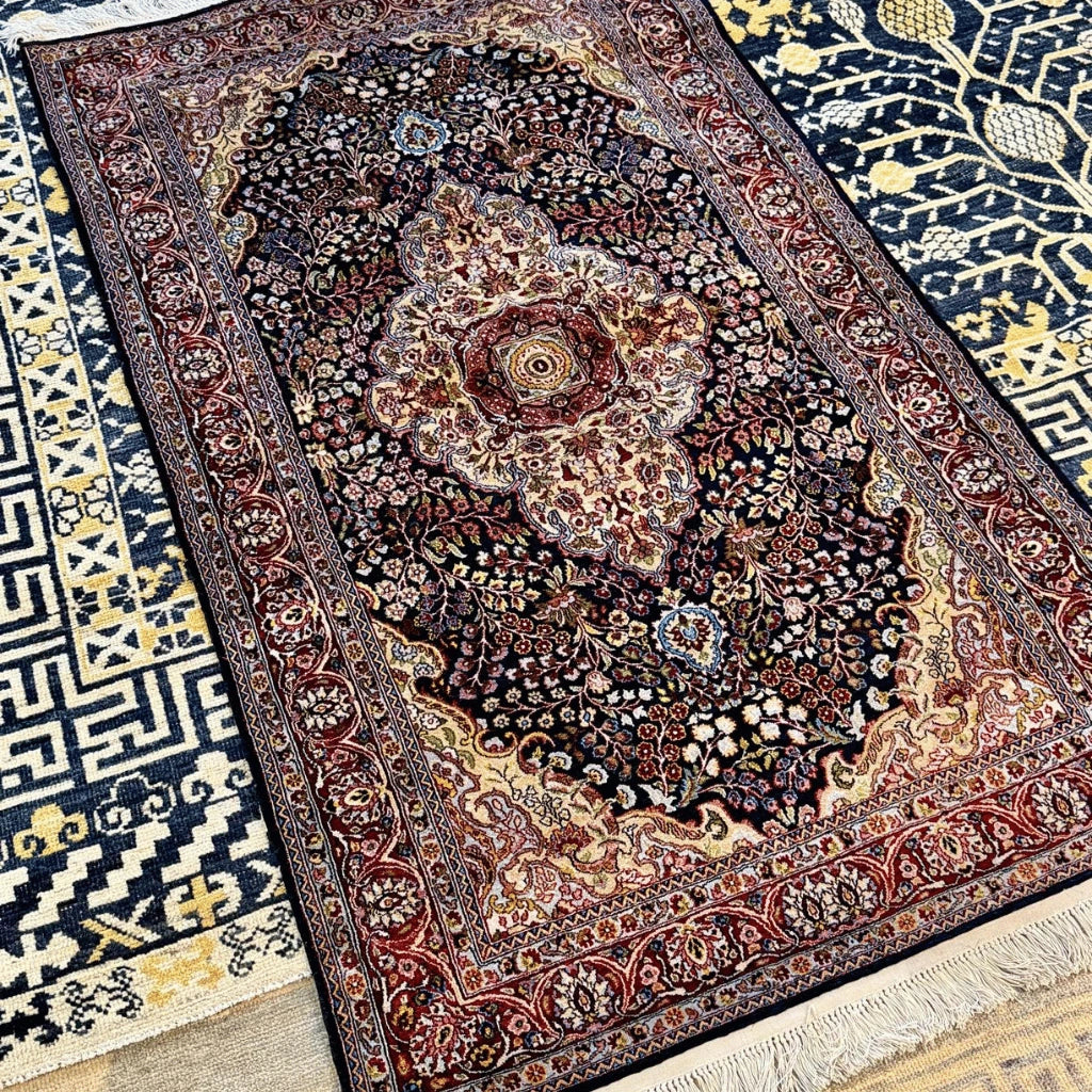 Hand-knotted Kashmiri silk rug with navy blue background, ornate cream central medallion, and red and gold floral patterns.