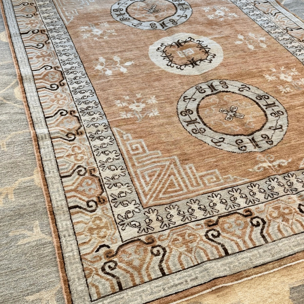 Traditional circular medallion on a tan and warm brown Afghan Khotan-inspired wool rug with dark decorative motifs.
