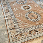 Traditional circular medallion on a tan and warm brown Afghan Khotan-inspired wool rug with dark decorative motifs.