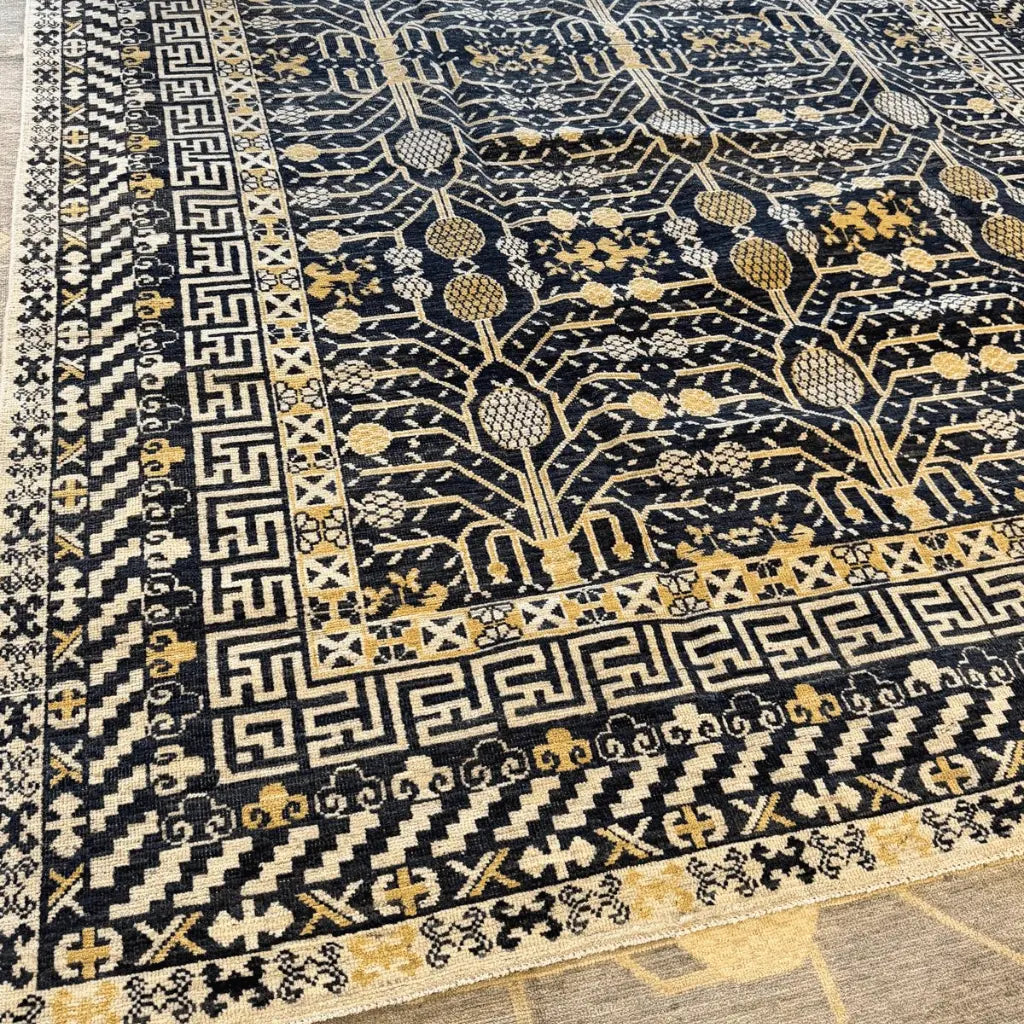 Full view of a large black Afghan Khotan handknotted wool rug with cream geometric borders and Tree of Life motifs.
