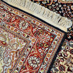 Detailed view of the Kashmiri silk rug's decorative red, cream, and gold floral border against a dark navy background.