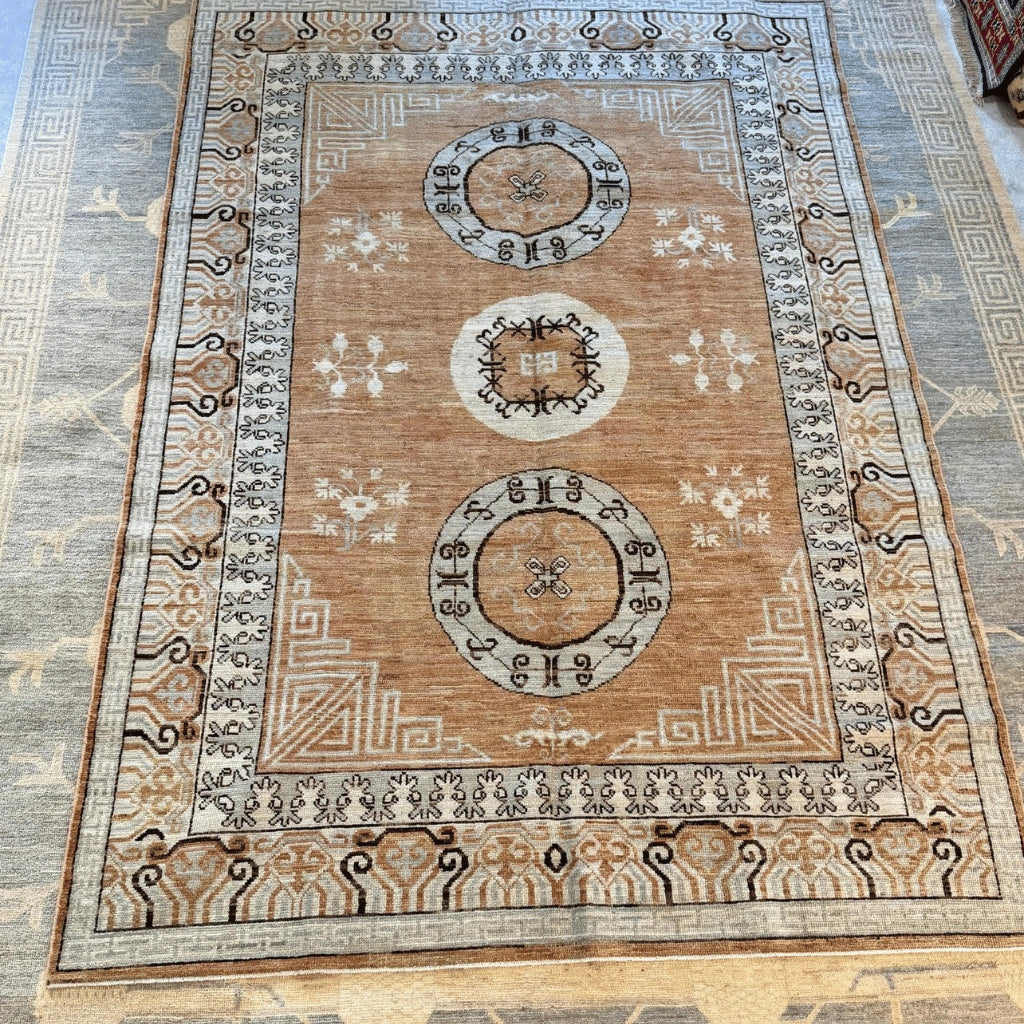 Full view of a traditional Afghan Khotan-inspired wool area rug with a warm brown field, cream borders, and three medallion motifs.