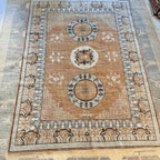 Full view of a traditional Afghan Khotan-inspired wool area rug with a warm brown field, cream borders, and three medallion motifs.