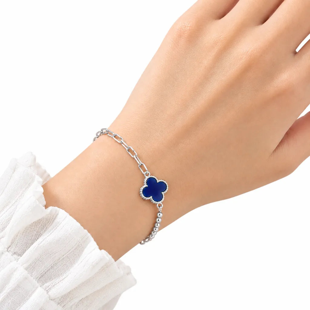Woman wearing sterling silver blue clover charm bracelet with paperclip chain and beaded detail on wrist with white sleeve
