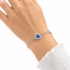 Woman wearing sterling silver double chain bracelet with blue heart halo center stone on wrist with white ribbed sleeve