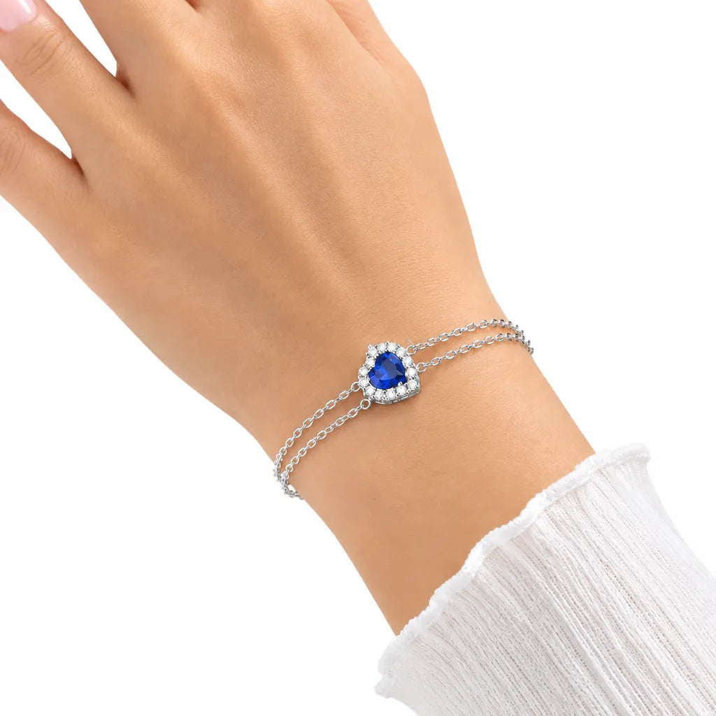 Woman wearing sterling silver double chain bracelet with blue heart halo center stone on wrist with white ribbed sleeve