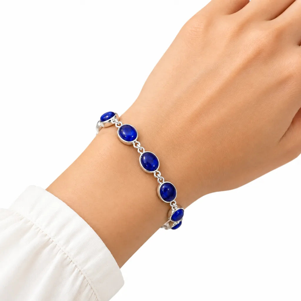 Woman wearing silver bracelet with oval blue cabochon gemstones on wrist with white sleeve