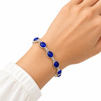 Woman wearing silver bracelet with oval blue cabochon gemstones on wrist with white sleeve