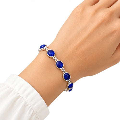 Woman wearing silver bracelet with oval blue cabochon gemstones on wrist with white sleeve