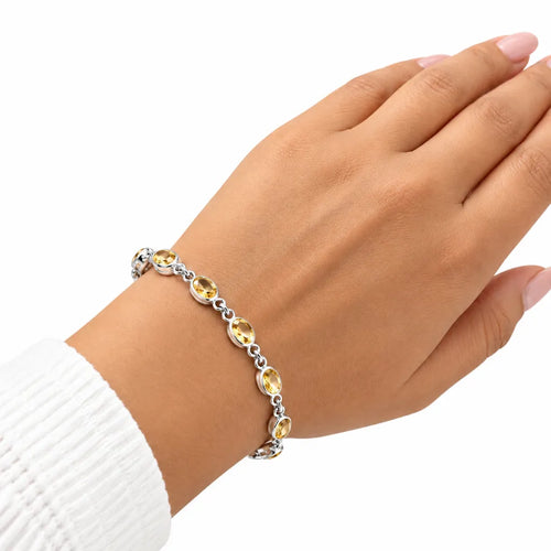 Woman wearing silver citrine gemstone bracelet with oval golden yellow stones on wrist with white knit sleeve