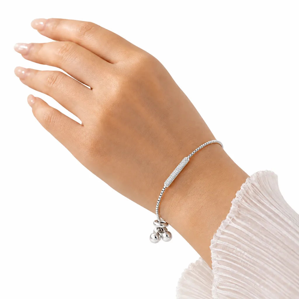 Woman wearing dainty sterling silver adjustable bar bracelet with sparkling cubic zirconia bar on wrist with white ruffle sleeve