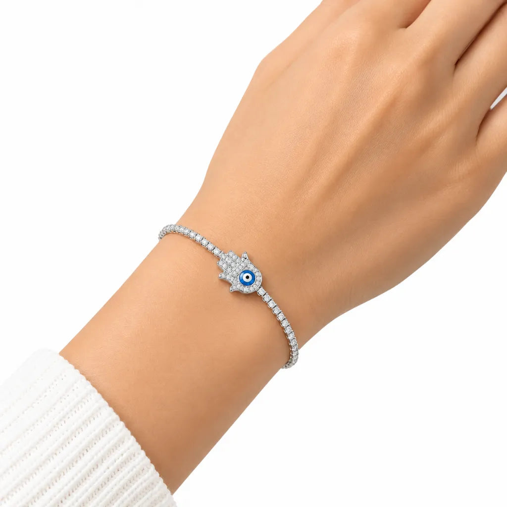 Woman wearing silver hamsa hand evil eye tennis bracelet with cubic zirconia on wrist with white knit sleeve