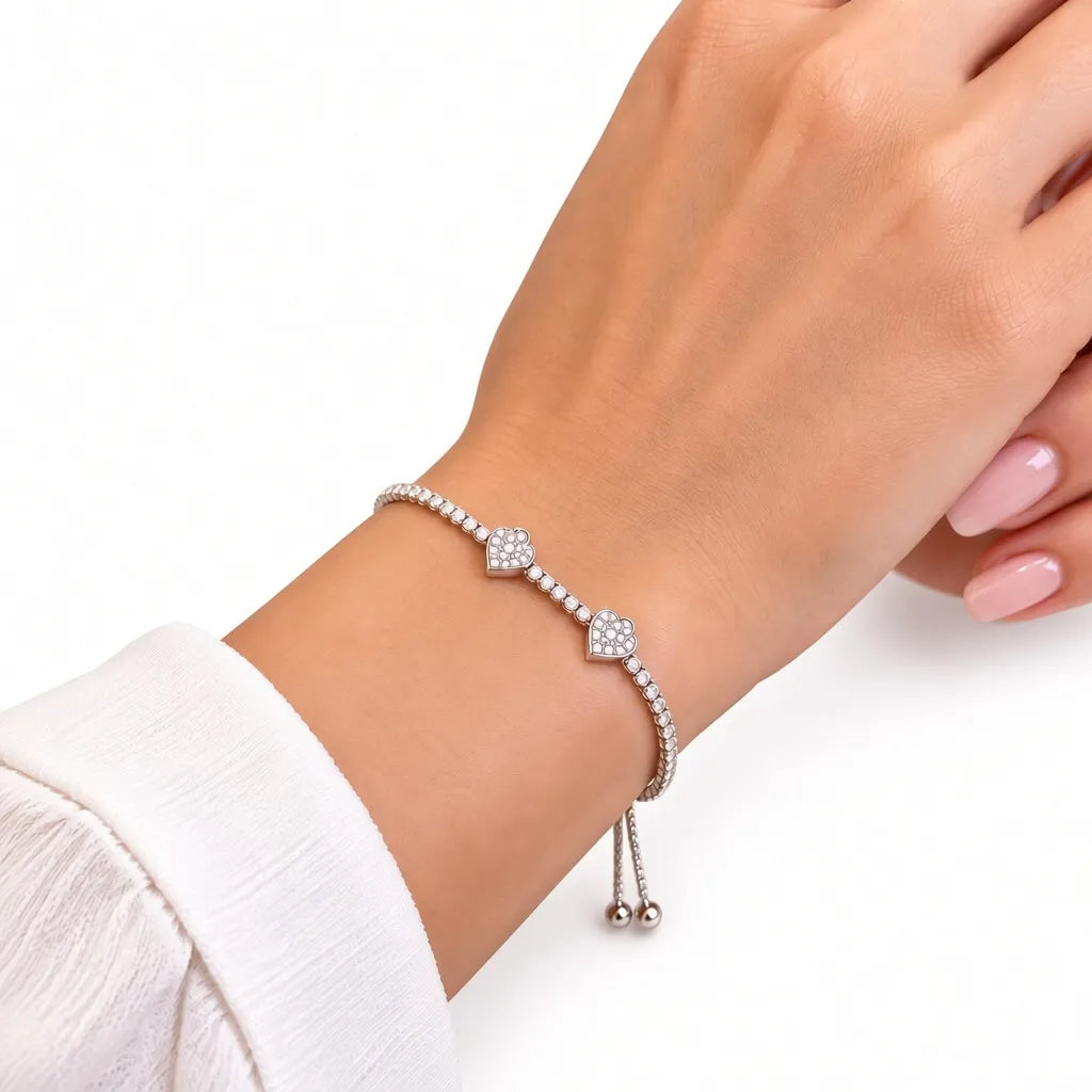 Woman wearing dainty silver double heart tennis bracelet with adjustable slider on wrist with white sleeve